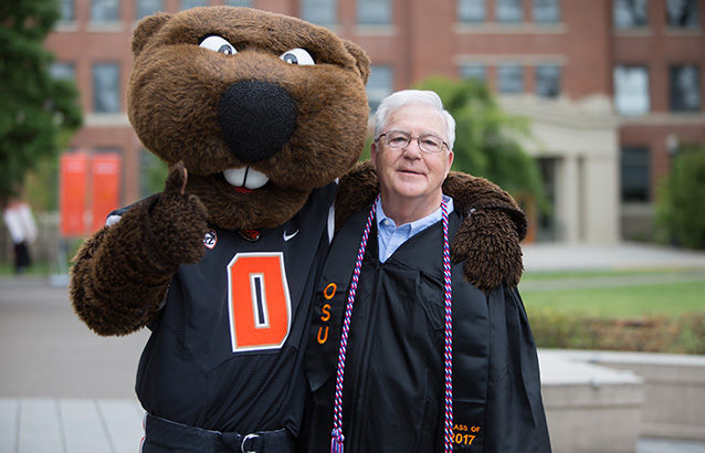 Oregon State's oldest 2017 graduate, Jerry Kight, poses with Benny the Beaver on graduation day.